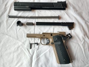 A field-stripped two-tone black and flat dark earth (FDE) Remington 1911-style semi-automatic pistol lying in its component parts on a wrinkled white fabric background