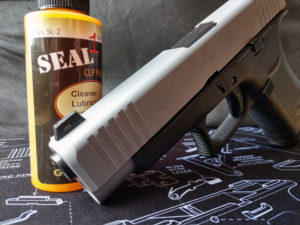 A two-tone silver and black Glock 48 9mm semi-automatic pistol propped against a yellow bottle of SEAL 1 non-toxic gun cleaning solution