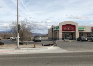 A homeless person lies beside a shopping cart near a street and a Papa John's parking lot in New Mexico