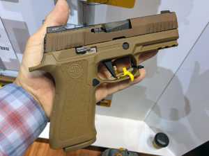 A white male in a red, white and blue plaid shirt displaying a Flat Dark Earth (FDE) SIG Sauer X-Compact 9mm compact concealed carry pistol in the flat of his open palm.