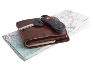 A brown leather wallet, a black kar key and fob and a folded paper road map lying on a white surface